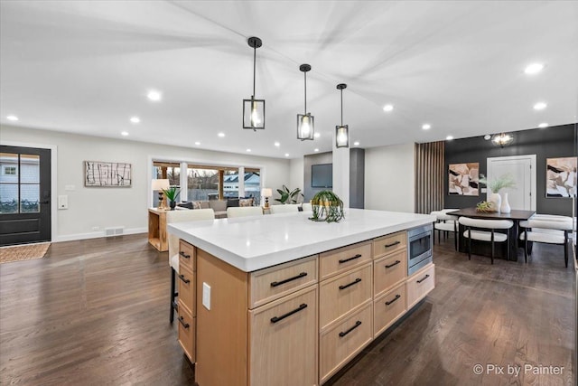 kitchen with light brown cabinets, stainless steel microwave, dark wood finished floors, and open floor plan