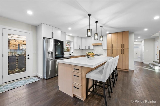 kitchen featuring a kitchen island, a kitchen breakfast bar, light countertops, stainless steel fridge with ice dispenser, and dark wood finished floors