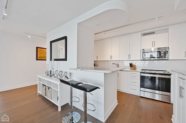 kitchen featuring appliances with stainless steel finishes, hardwood / wood-style floors, decorative backsplash, and white cabinets