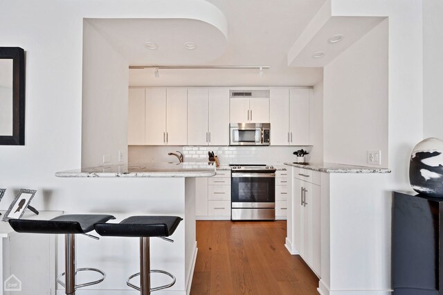 kitchen featuring white cabinetry, stainless steel appliances, kitchen peninsula, and light stone countertops