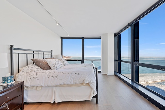 bedroom with a water view, floor to ceiling windows, and light hardwood / wood-style floors