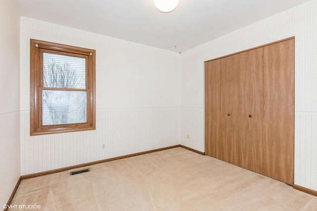 unfurnished bedroom with wallpapered walls, carpet, visible vents, and a closet