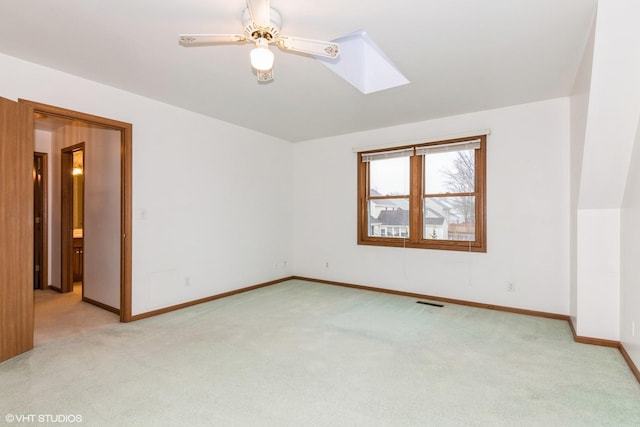 spare room with a skylight, light colored carpet, ceiling fan, and baseboards