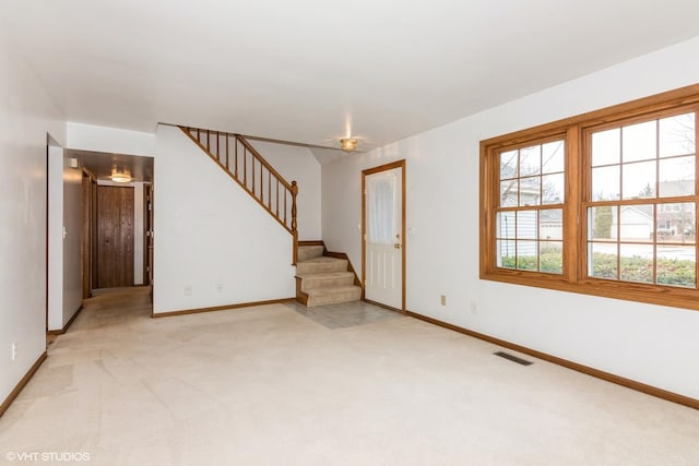 unfurnished living room with light colored carpet, visible vents, baseboards, and stairs