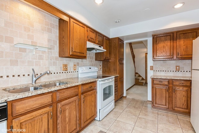 kitchen with light tile patterned floors, under cabinet range hood, white appliances, a sink, and brown cabinets