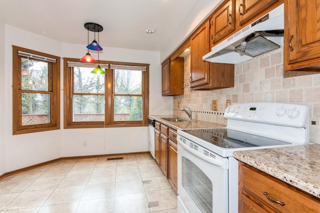 kitchen featuring white appliances, under cabinet range hood, brown cabinetry, and a sink