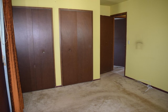 unfurnished bedroom with light colored carpet and two closets