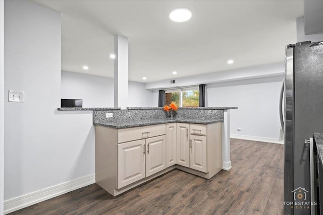 kitchen featuring dark stone countertops, kitchen peninsula, dark hardwood / wood-style floors, and stainless steel fridge