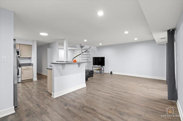 kitchen with cream cabinetry, stone counters, wood-type flooring, and a breakfast bar