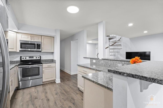 kitchen with light hardwood / wood-style flooring, appliances with stainless steel finishes, cream cabinets, a breakfast bar, and stone counters