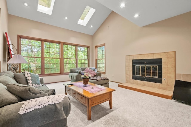 living room with a tiled fireplace, carpet floors, high vaulted ceiling, and a skylight