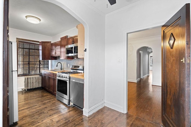 kitchen featuring appliances with stainless steel finishes, dark hardwood / wood-style floors, radiator heating unit, wooden counters, and decorative backsplash