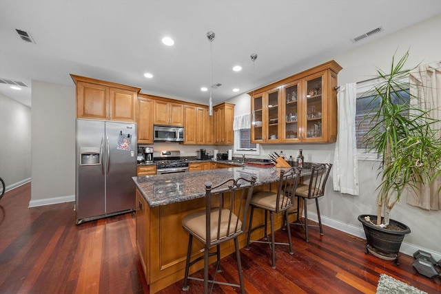 kitchen featuring appliances with stainless steel finishes, dark stone countertops, hanging light fixtures, a kitchen breakfast bar, and dark hardwood / wood-style floors