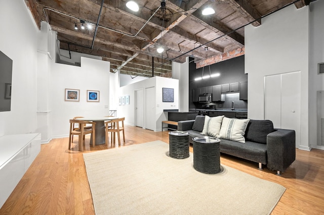 living room with a high ceiling, rail lighting, sink, and light wood-type flooring