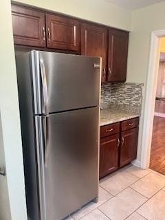 kitchen featuring light tile patterned flooring, dark brown cabinetry, stainless steel fridge, and tasteful backsplash