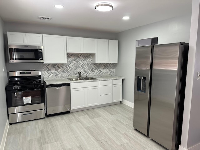 kitchen featuring appliances with stainless steel finishes, sink, white cabinetry, light stone countertops, and decorative backsplash