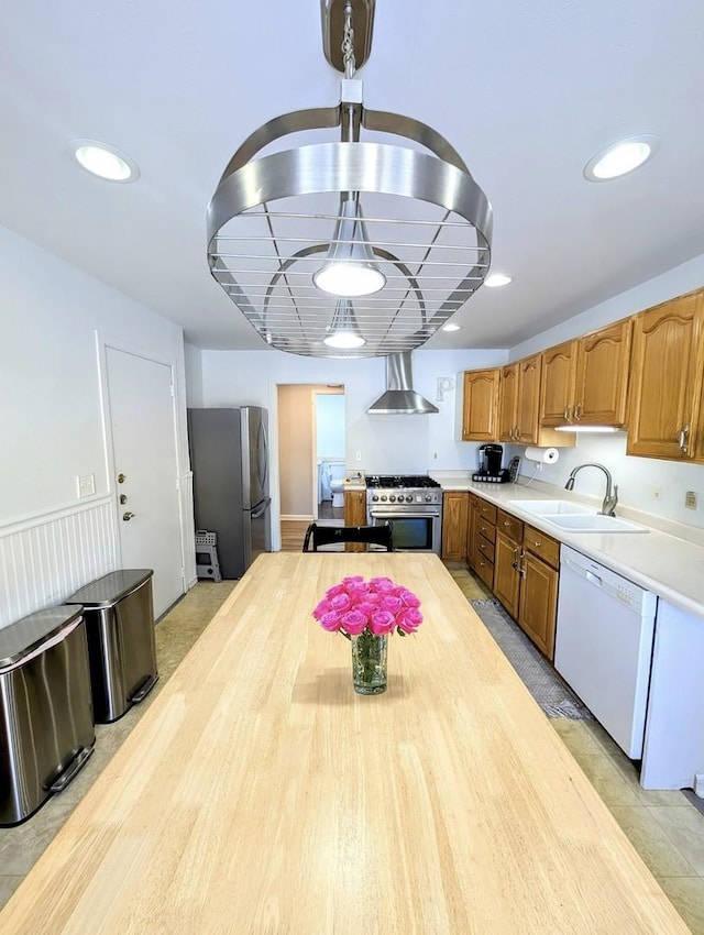 kitchen featuring pendant lighting, stainless steel appliances, sink, and wall chimney range hood