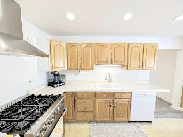 kitchen with light brown cabinetry, sink, white dishwasher, gas stove, and wall chimney range hood