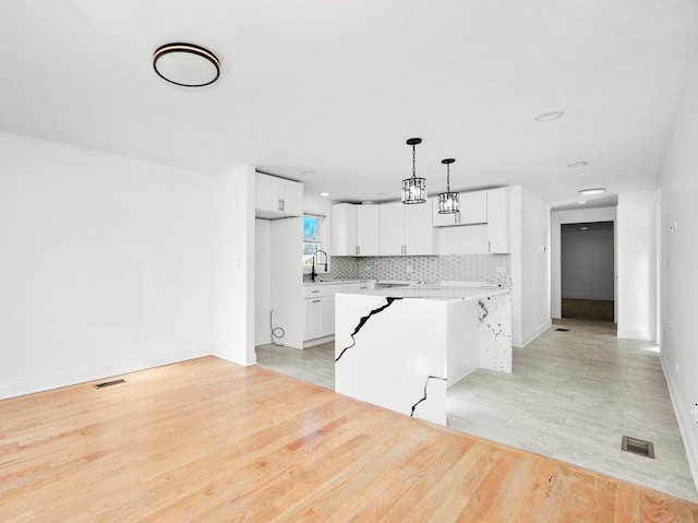 kitchen featuring sink, white cabinetry, decorative light fixtures, light wood-type flooring, and backsplash