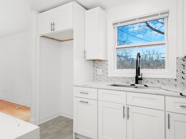 kitchen with white cabinetry, sink, backsplash, and light stone countertops