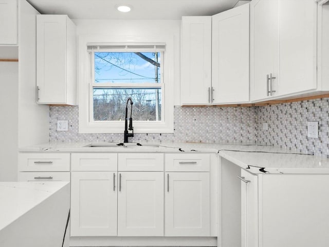 kitchen with white cabinetry, light stone counters, sink, and tasteful backsplash