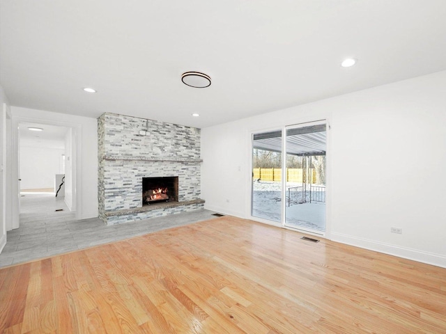 unfurnished living room featuring a stone fireplace and light hardwood / wood-style floors