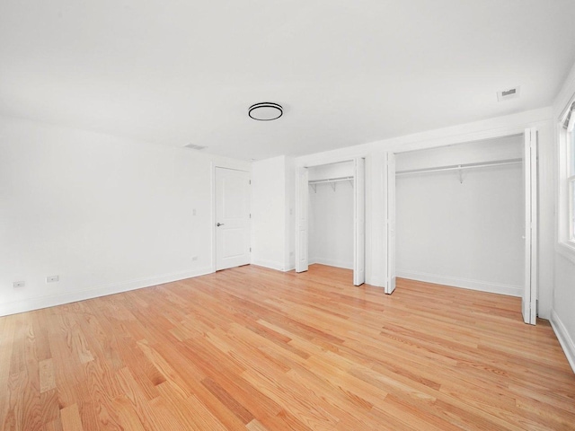 unfurnished bedroom featuring multiple closets and light wood-type flooring