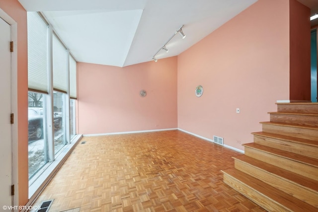 empty room with a wall of windows, rail lighting, and light parquet floors