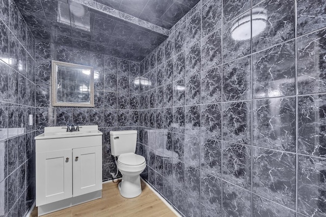 bathroom with wood-type flooring, tile walls, vanity, and toilet