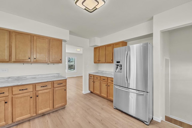 kitchen with light stone counters, light hardwood / wood-style floors, and stainless steel fridge with ice dispenser