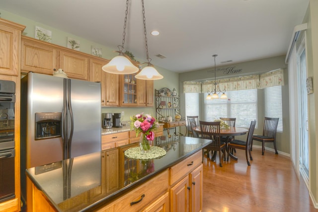 kitchen with stainless steel fridge, black oven, light hardwood / wood-style floors, a kitchen island, and decorative light fixtures