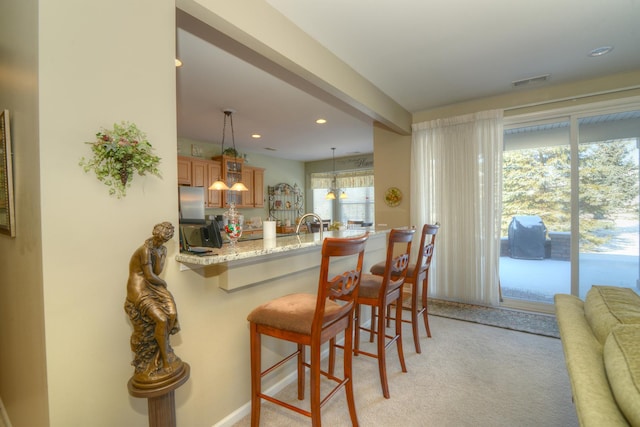 kitchen featuring light stone counters, a kitchen bar, decorative light fixtures, light colored carpet, and kitchen peninsula