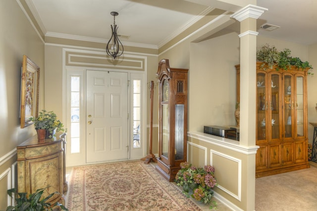 foyer entrance with decorative columns, ornamental molding, and light colored carpet