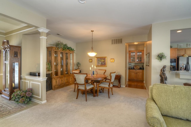 carpeted dining room featuring decorative columns and ornamental molding