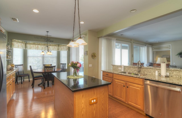 kitchen with sink, hanging light fixtures, stainless steel appliances, a center island, and light stone counters