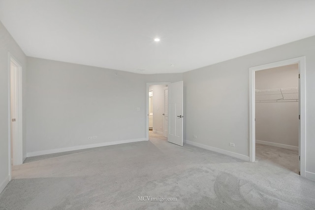 unfurnished bedroom with a walk in closet, light colored carpet, and a closet