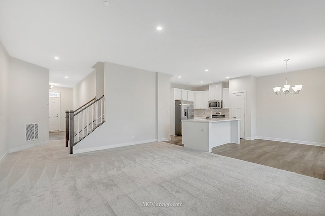 kitchen featuring pendant lighting, white cabinets, a chandelier, stainless steel appliances, and a center island with sink