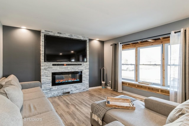 living room with a stone fireplace and light wood-type flooring