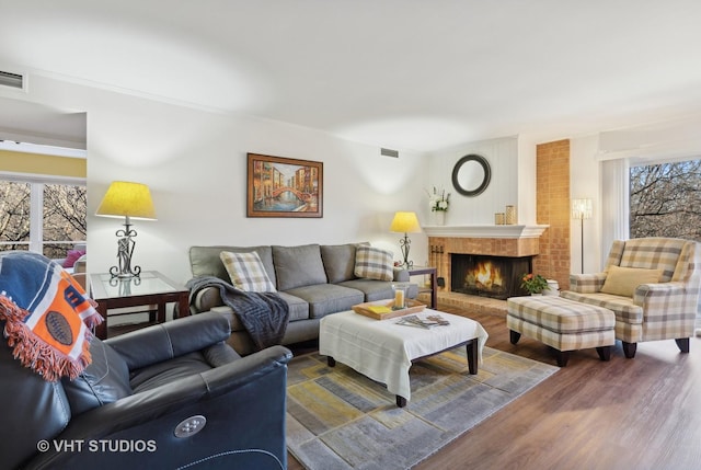 living room with wood-type flooring, plenty of natural light, and a brick fireplace