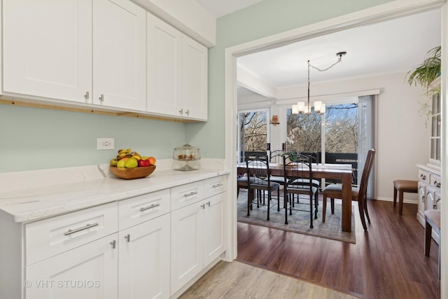 kitchen with white cabinetry, an inviting chandelier, hanging light fixtures, light stone countertops, and light hardwood / wood-style floors