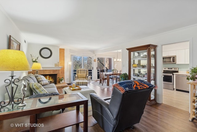 living room featuring ornamental molding, a brick fireplace, a notable chandelier, and light hardwood / wood-style floors