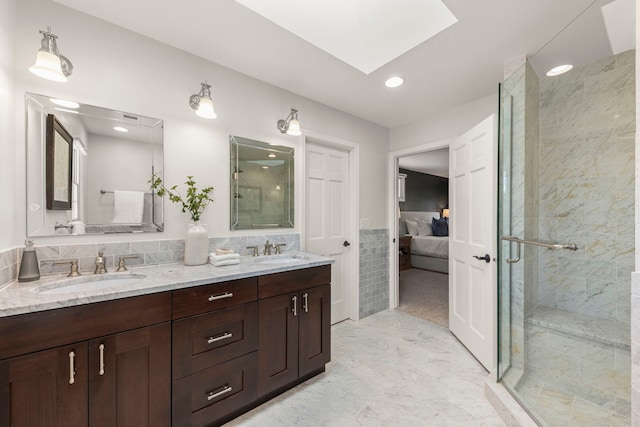 bathroom with tile walls, vanity, a skylight, and a shower with shower door