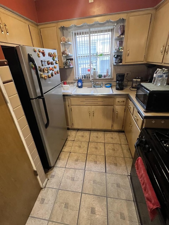 kitchen with light tile patterned flooring, light brown cabinetry, stainless steel refrigerator, sink, and gas range