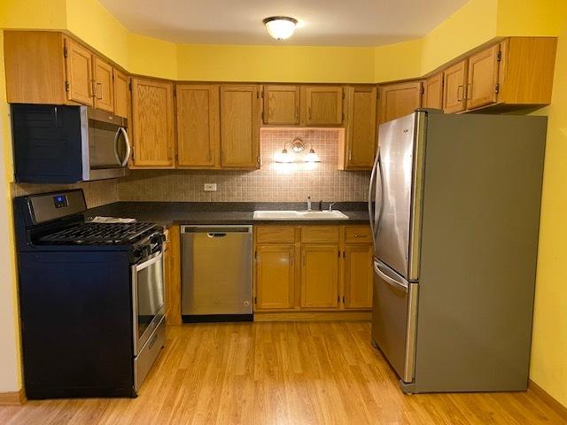 kitchen with decorative backsplash, appliances with stainless steel finishes, sink, and light hardwood / wood-style flooring