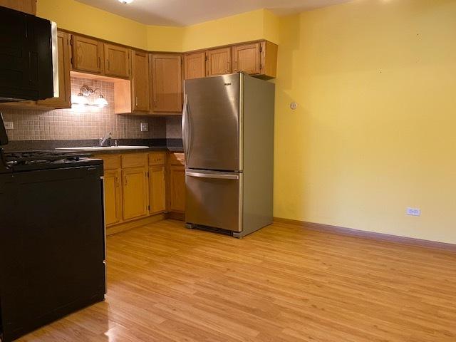 kitchen featuring sink, stainless steel refrigerator, black range, light hardwood / wood-style floors, and decorative backsplash