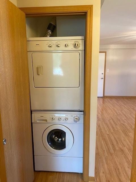 washroom with stacked washer and dryer and light wood-type flooring