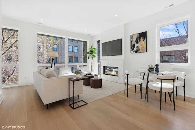 living room with a high end fireplace and light hardwood / wood-style flooring