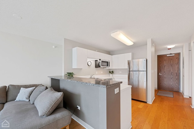 kitchen with sink, appliances with stainless steel finishes, kitchen peninsula, light hardwood / wood-style floors, and white cabinets