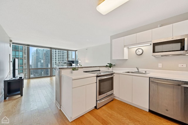 kitchen with sink, white cabinets, a wall of windows, kitchen peninsula, and stainless steel appliances