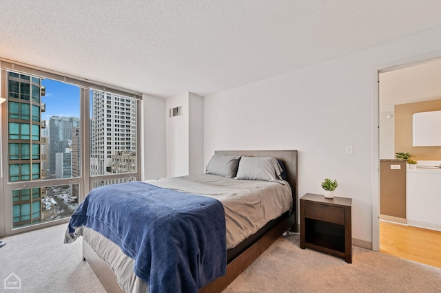 bedroom featuring light carpet, a textured ceiling, and a wall of windows